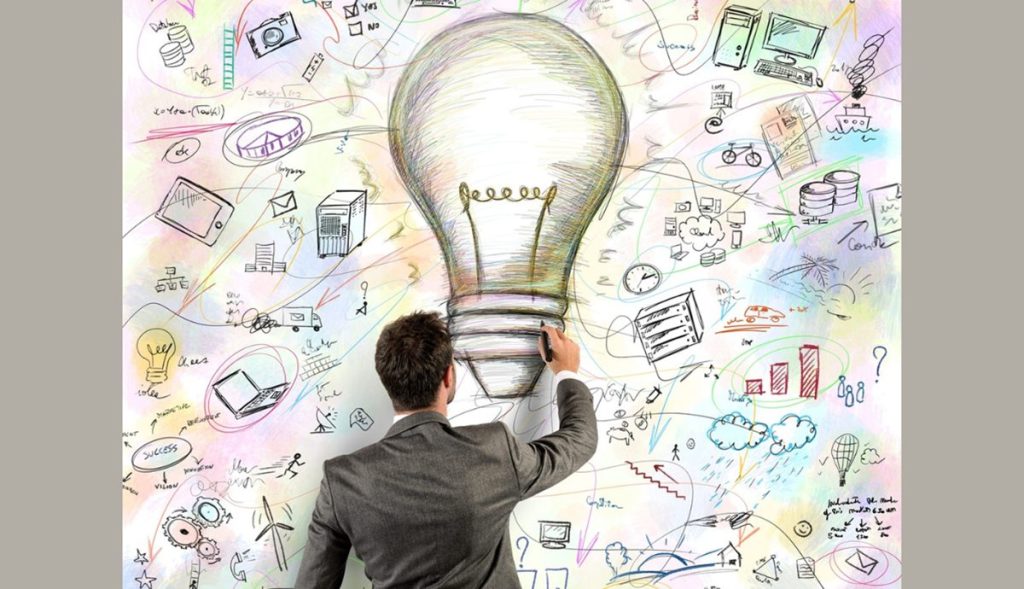 Un professionista di spalle disegna una grande lampadina circondata da icone di tecnologia energetica e sostenibilità.
