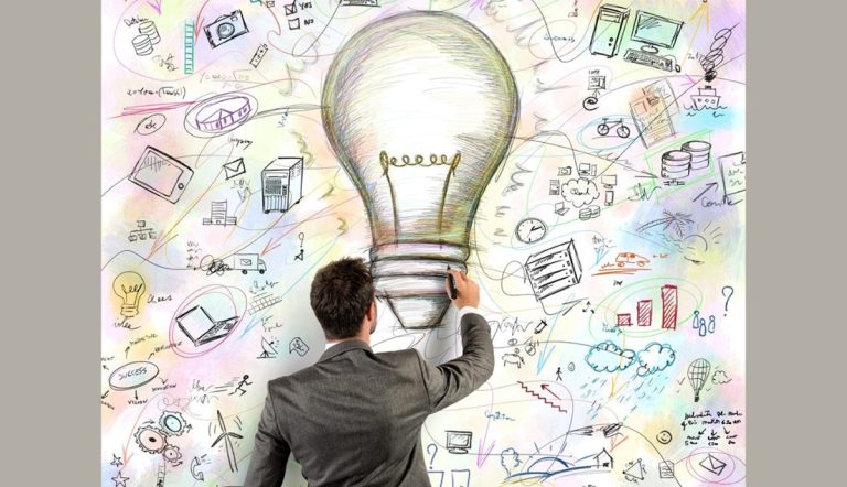 Un professionista di spalle disegna una grande lampadina circondata da icone di tecnologia energetica e sostenibilità.