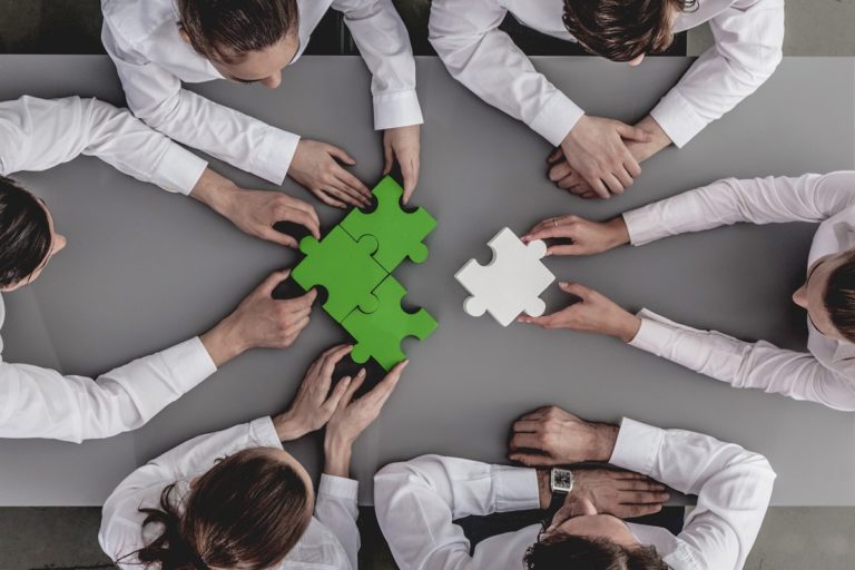 Un team di professionisti lavora insieme per completare un puzzle, simbolo della rendicontazione di sostenibilità e della collaborazione strategica nel reporting aziendale