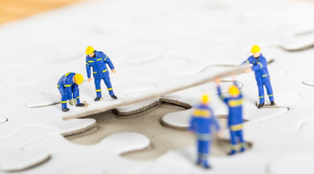 Lavoratori con dispositivi di protezione individuale che completano un puzzle, simbolo del coordinamento e della strategia nazionale per la salute e sicurezza sul lavoro.