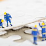 Lavoratori con dispositivi di protezione individuale che completano un puzzle, simbolo del coordinamento e della strategia nazionale per la salute e sicurezza sul lavoro.