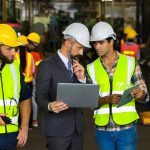 Professionista RSPP in abito scuro con laptop monitora e si confronta con tecnici e operatori.
