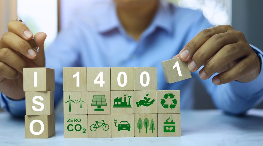 Persona che compone con blocchi di legno il logo ISO 14001 e icone di sostenibilità ambientale.