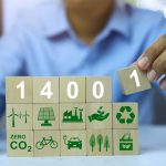 Persona che compone con blocchi di legno il logo ISO 14001 e icone di sostenibilità ambientale.